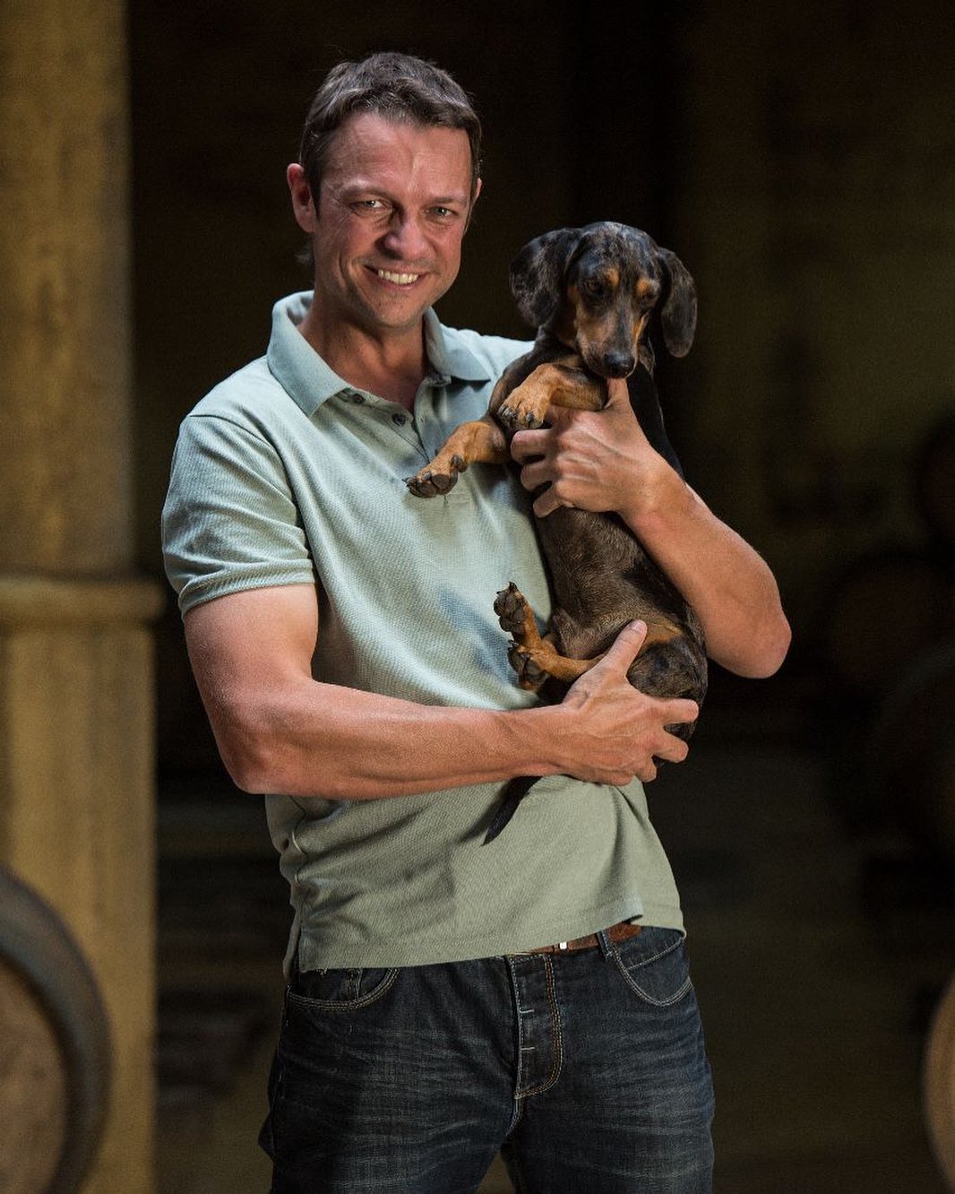 Andries de Klerk, Morgenhof Estate cellar master, holding a dachshund in the wine cellar